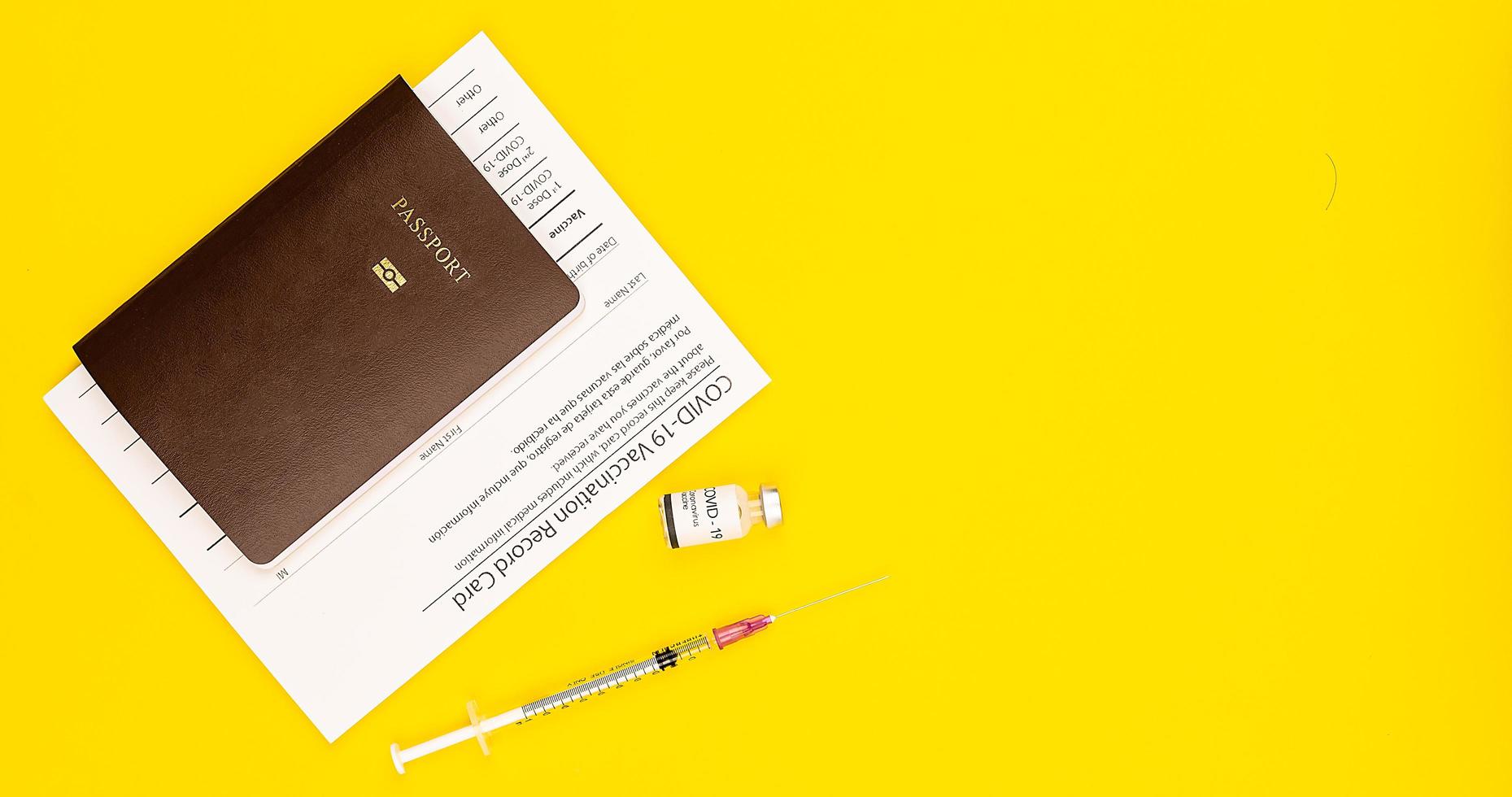 covid-19 vaccinerat journalkortsintyg och pass med coronavirusvaccinflaska och spruta ihopsatt på gul bakgrund med kopia utrymme. ovanifrån och platt låg skott foto