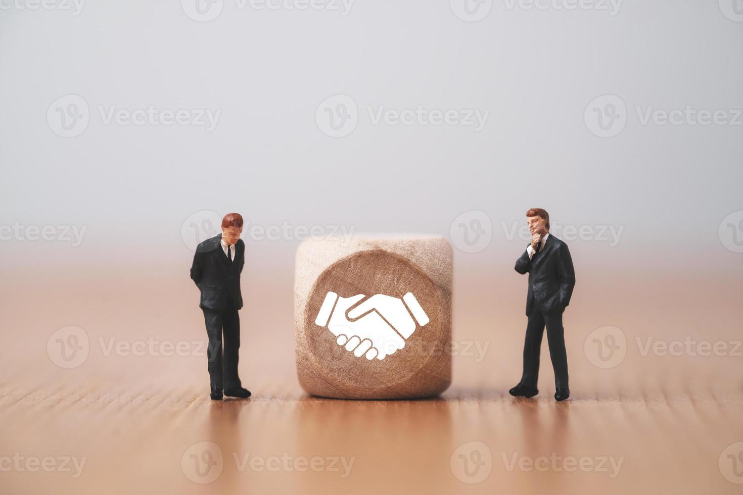 affärsmän står och tänker med handskakning vilken utskriftsskärm på träkubblock framför mänsklig ikon för affärsuppgörelse och avtalskoncept. foto