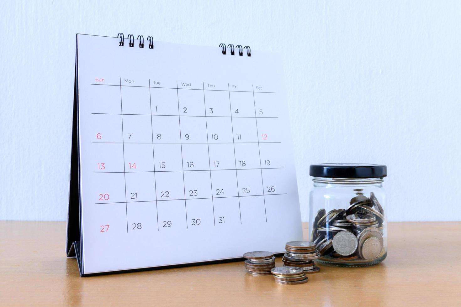 kalender med dagar och mynt i burken på träbord foto