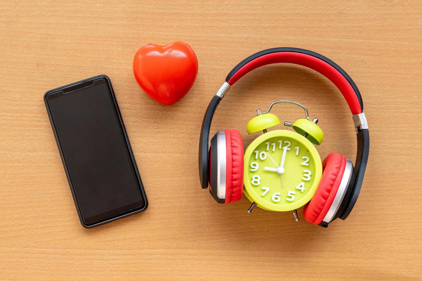 hörlurar och väckarklocka och smartphone och rött hjärta på trä skrivbord. musikaliskt koncept foto