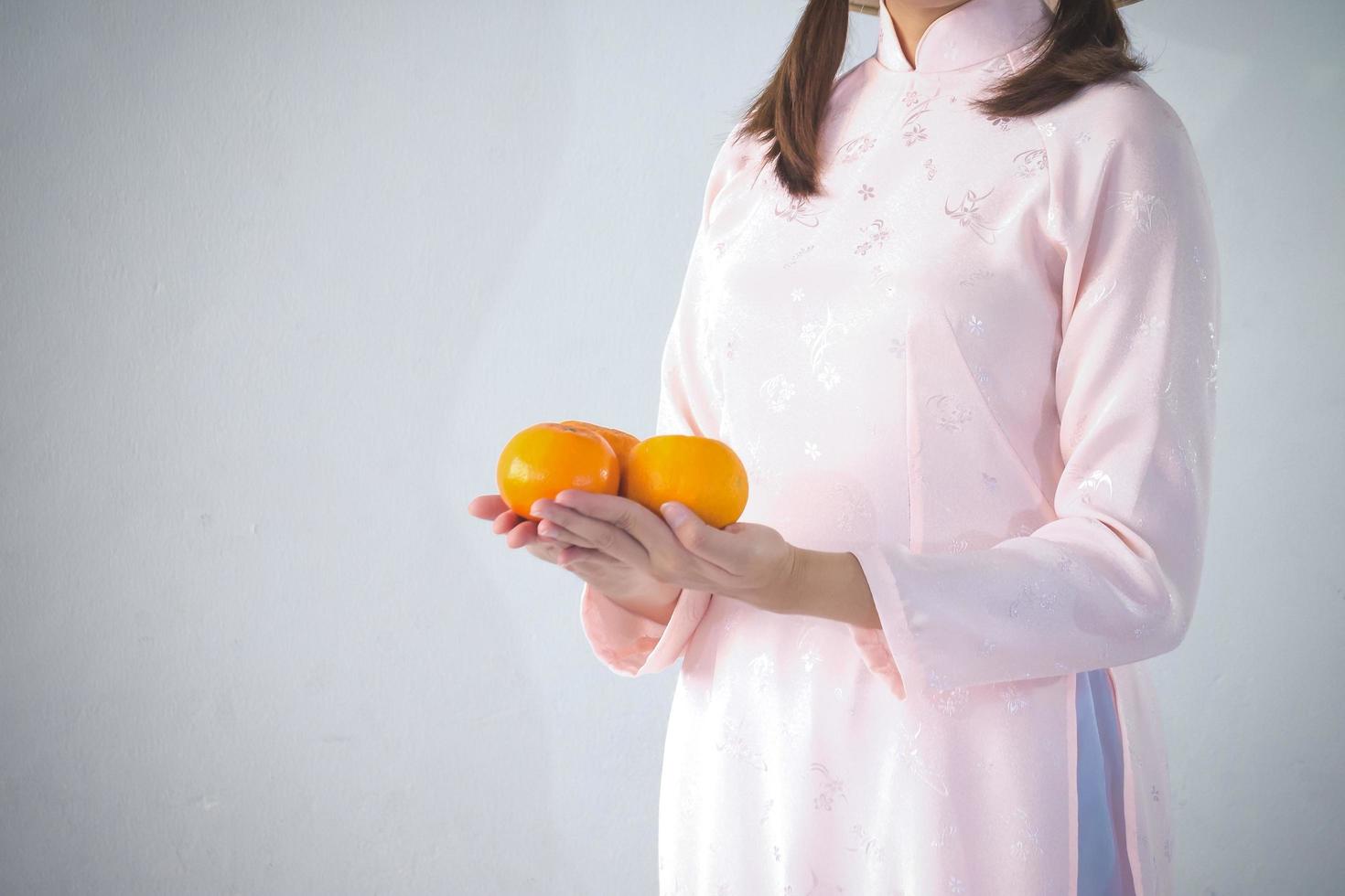 vacker kvinna i rosa klänning och vietnamhatt som håller orange foto