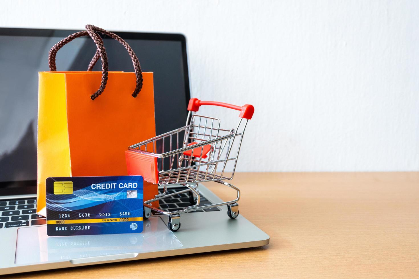 kreditkort och vagn stormarknad och orange papperspåse på träbord. shopping koncept foto