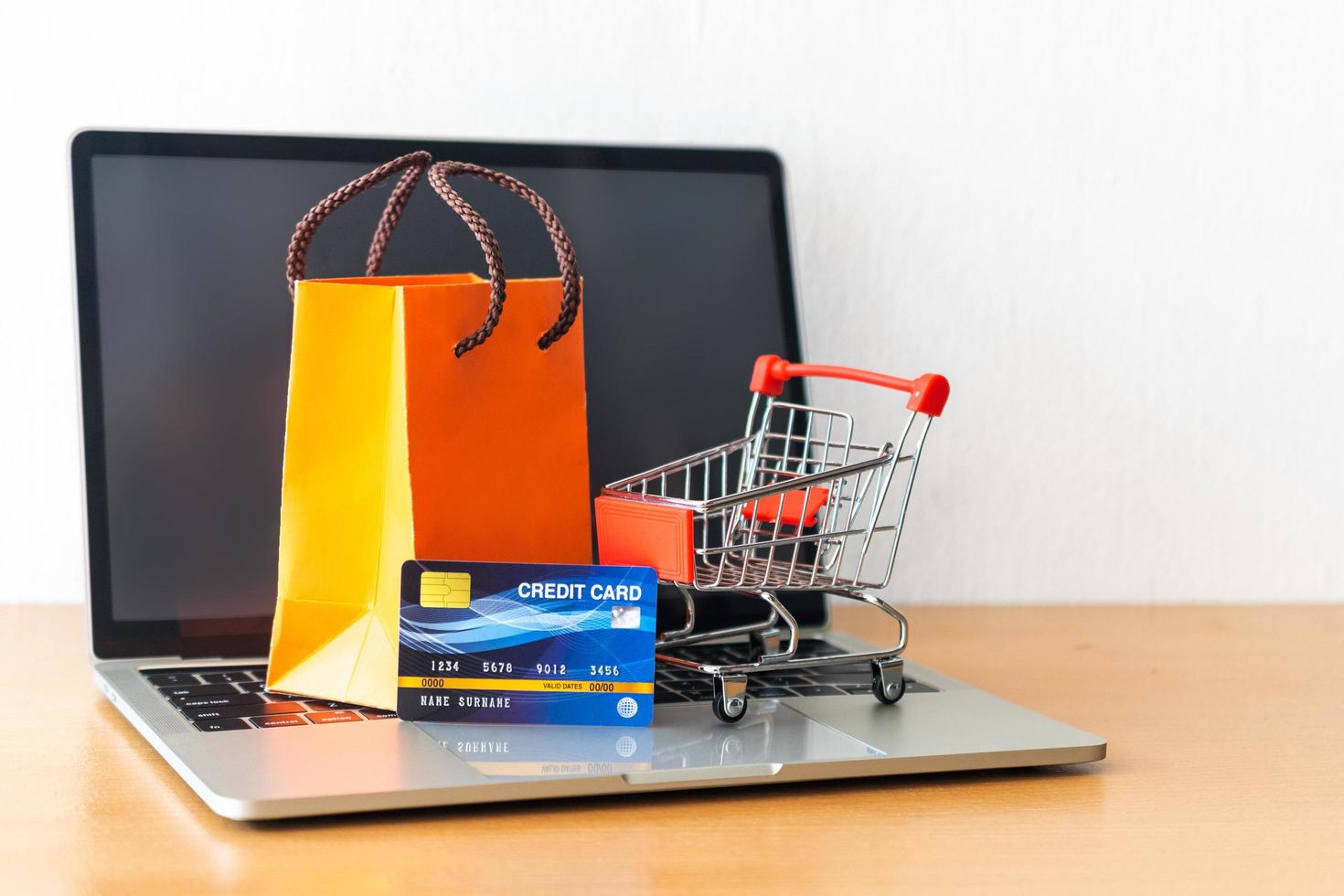 kreditkort och vagn stormarknad och orange papperspåse på träbord. shopping koncept foto
