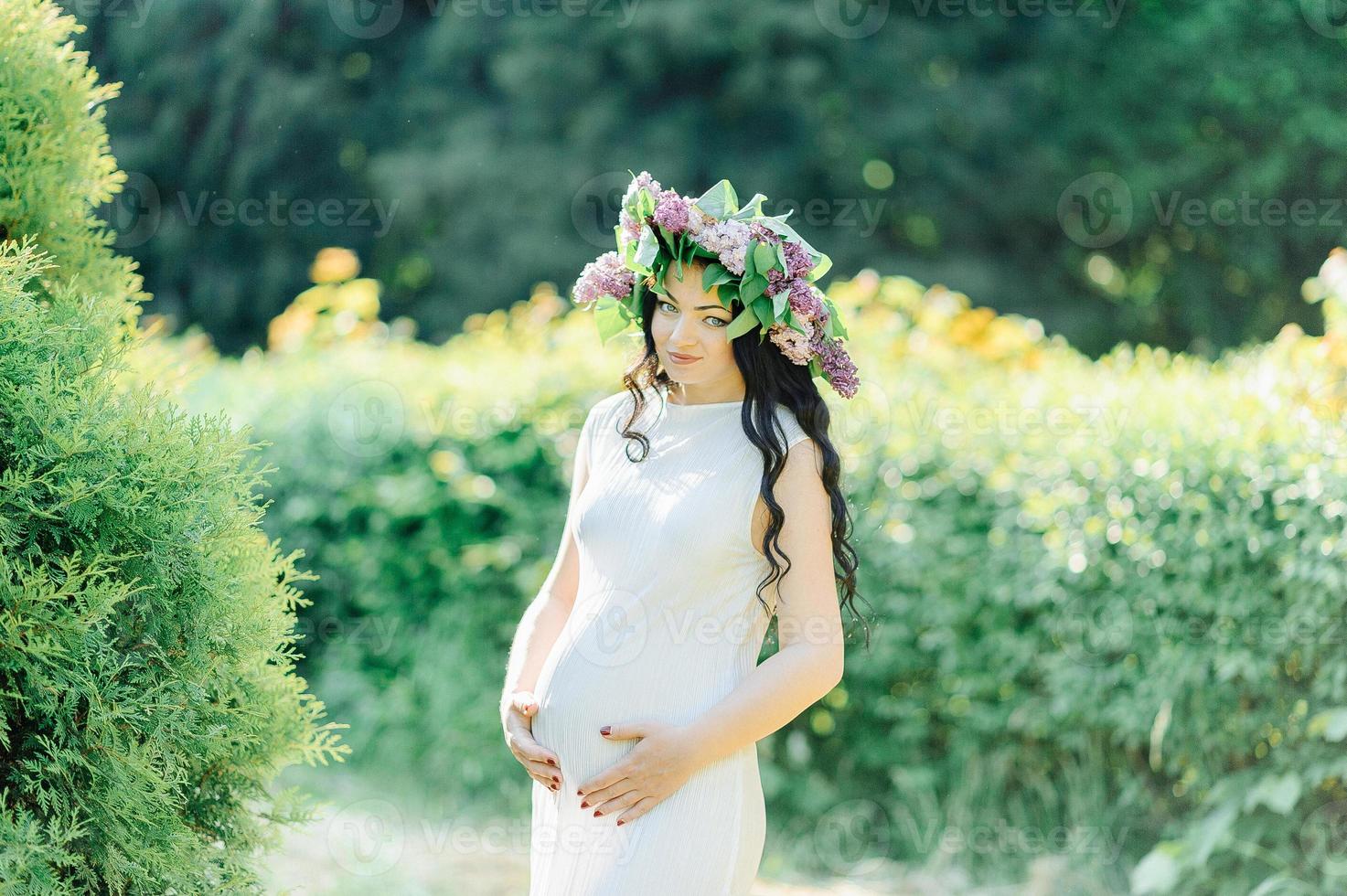 ung gravid kvinna i våren lila blommande trädgård. romantisk look med stråhatt. kaukasisk kvinna med långa bruna hår. begreppet nytt liv i naturen och människan. väntan på bebis foto