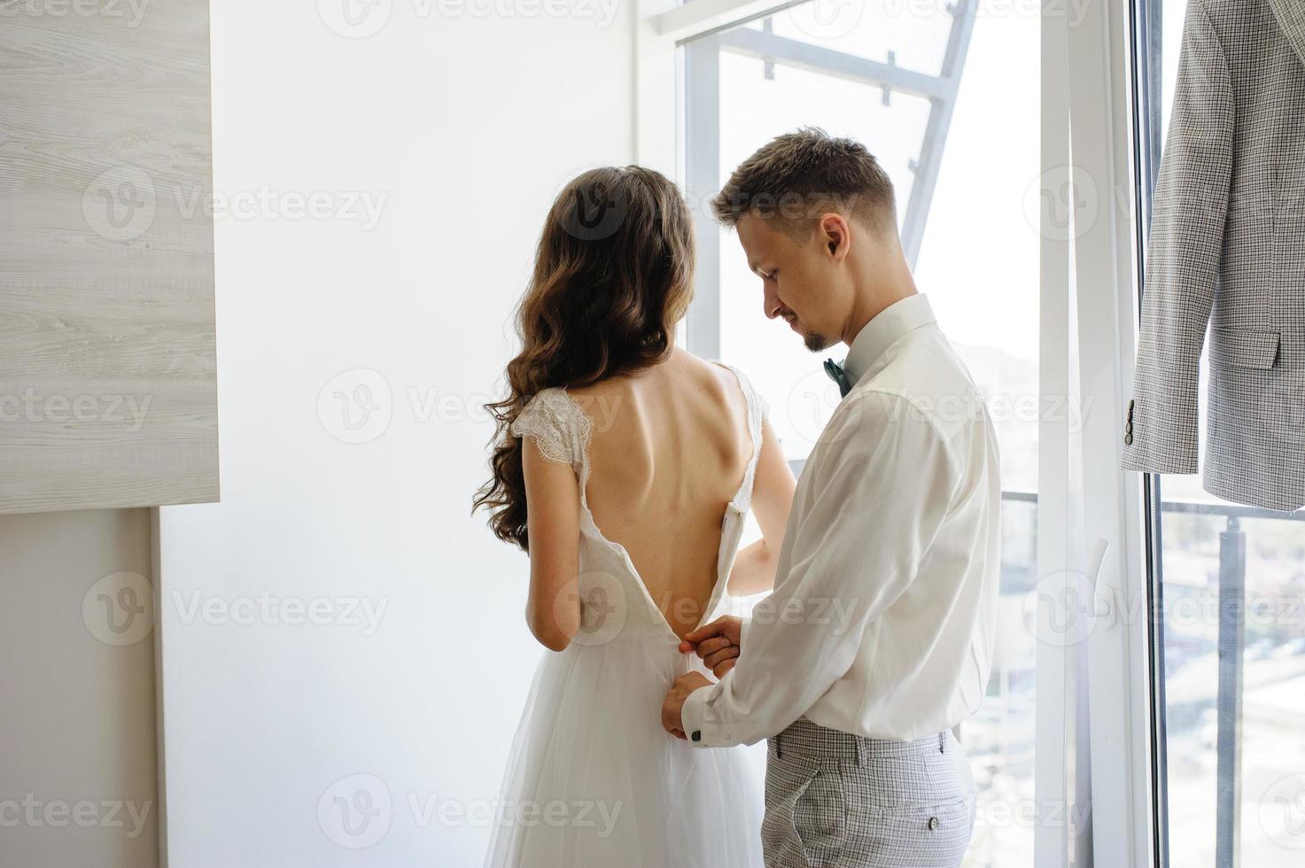 brudgummen hjälper till att fästa klänningen på sin brud. foto