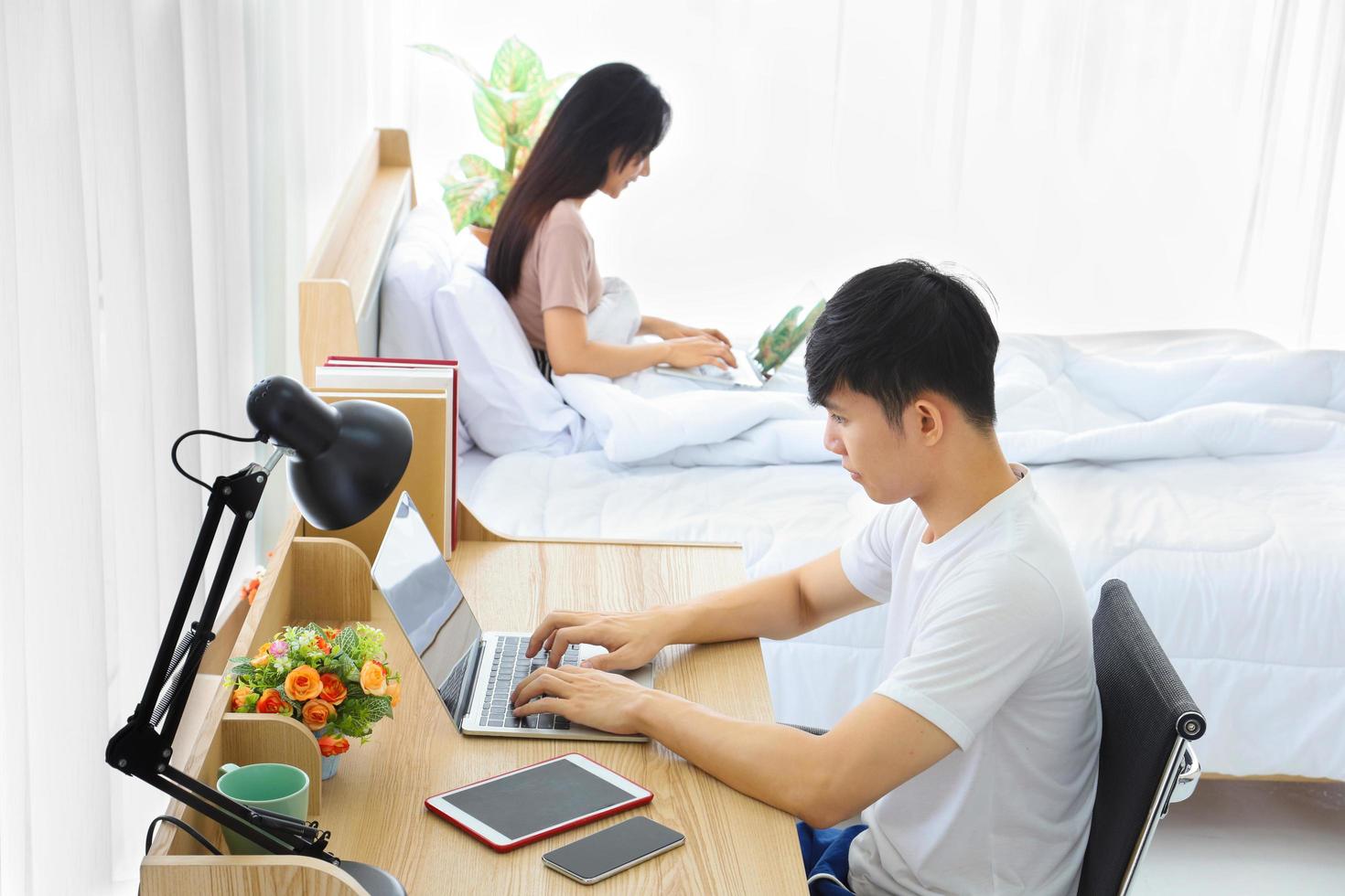 Ungt par som arbetar online hemifrån i sovrummet tillsammans som karantän för ny normal och social distanspolicy foto