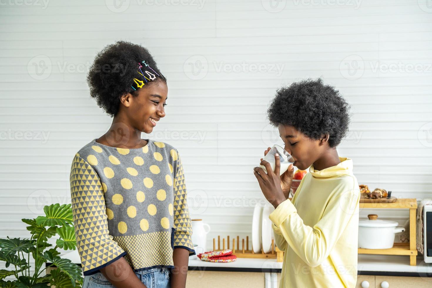 söta små barn som äter frukost med mjölk i köket, afrikansk amerikansk söt pojke som dricker mjölk med sin syster, mat och dryck koncept med kopia utrymme foto