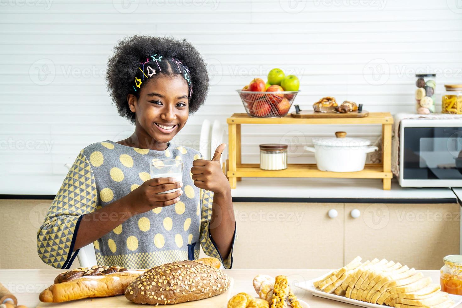 ung glad kvinna afroamerikanskt afrohår dricker ett glas mjölk hemma nöjd med stort leende gör ok tecken, tummen upp med fingrar, utmärkt tecken foto