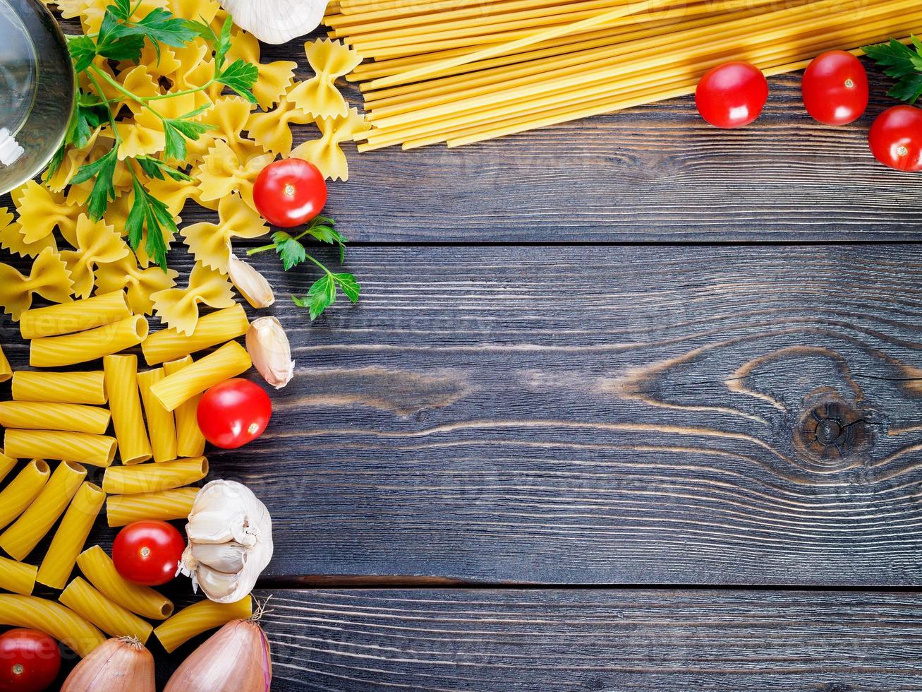 pasta, tomater, schalottenlök, vitlök, persilja på mörk träbakgrund, ovanifrån, kopieringsutrymme. foto