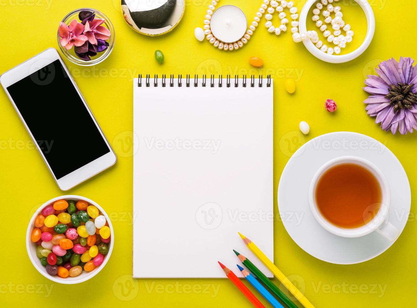 myshörna för en tjej med en anteckningsbok, smartphone, blommor, smycken och godis. skrivbord för kreativitet, idéer, kreativitet, drömmar. ljusgul bakgrund, ovanifrån, platt låg, tom plats för text. foto