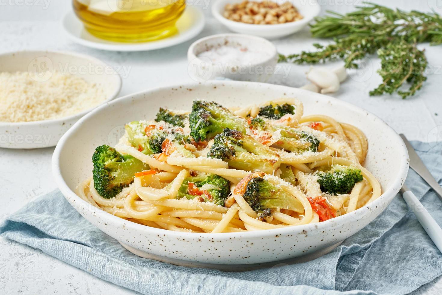 spaghettipasta med broccoli, bucatini med paprika, vitlök, pinjenötter. ljus vitt bord. foto