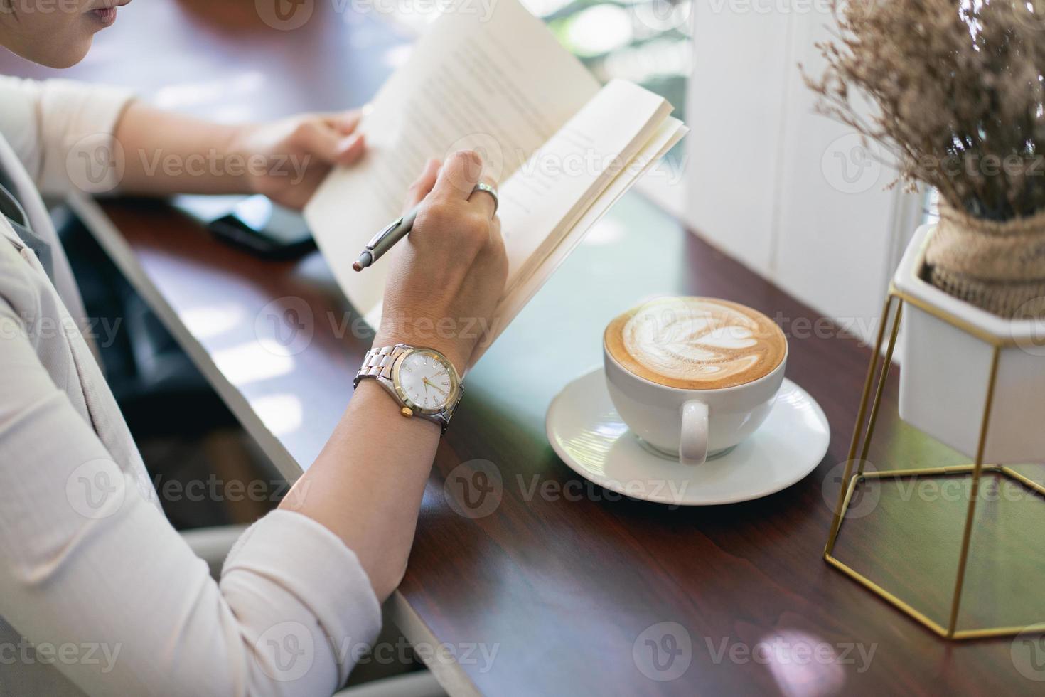 kvinna som bär klockor och skriver dagbok på liten anteckningsbok på inomhuscafé. kvinna anteckningar och dricka kaffe på café. foto