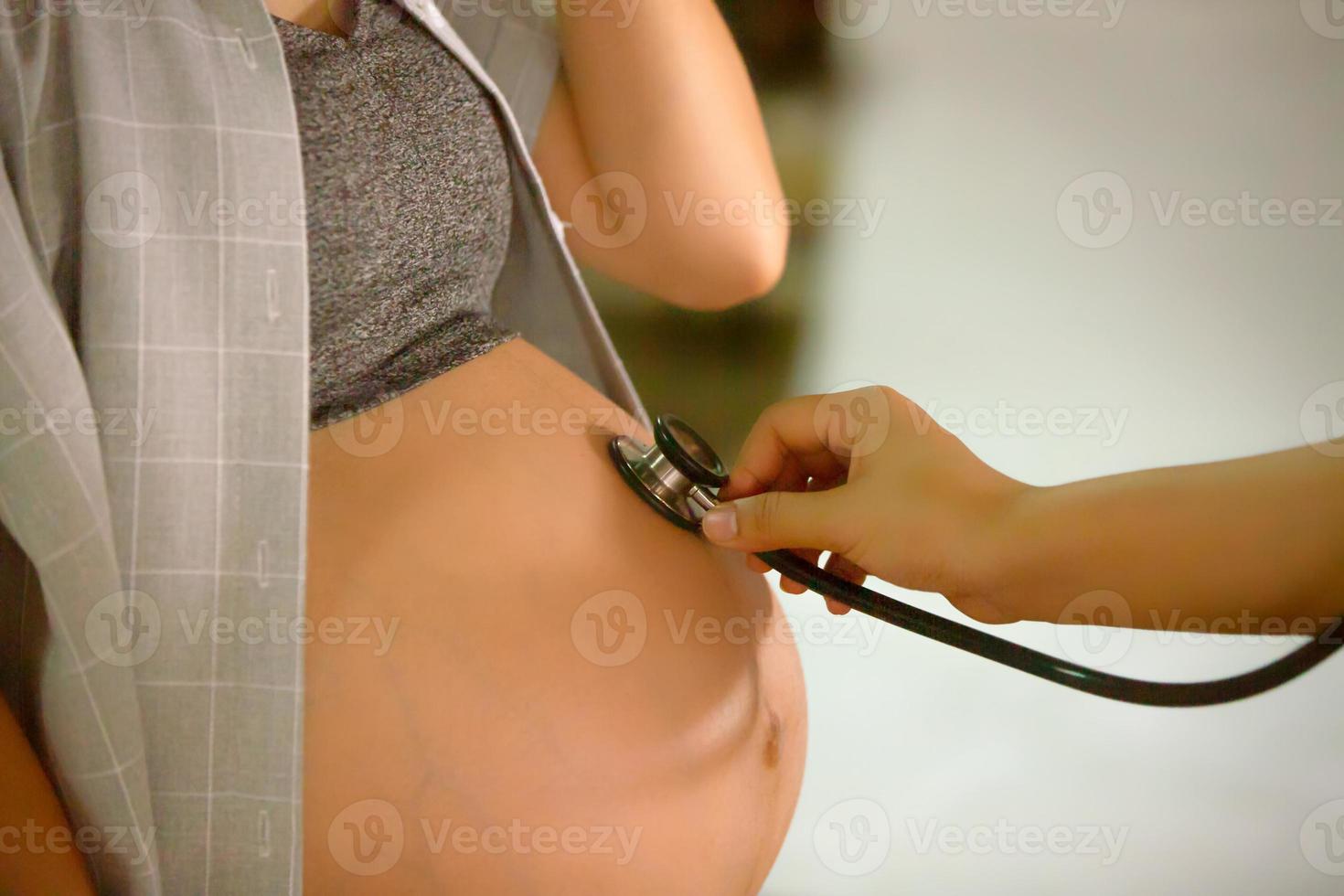 mittsektionsporträtt av en oigenkännlig kvinna under de sista månaderna av graviditeten som håller hennes stora mage försiktigt foto
