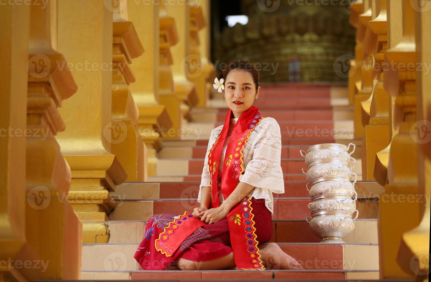 ung asiatisk flicka i traditionell burmesisk kostym håller skål med ris till hands på gyllene pagoden i myanmar tempel. myanmar kvinnor som håller blommor med burmesisk traditionell klänning som besöker ett buddhistiskt tempel foto