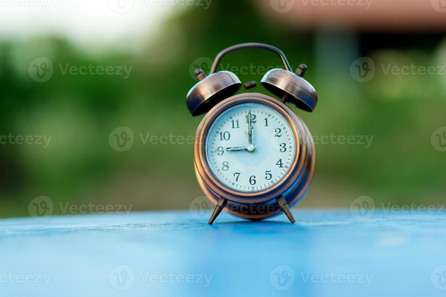 gyllene väckarklocka bild placerad på ett blått bord, grön bakgrund punktligt koncept med kopia utrymme foto