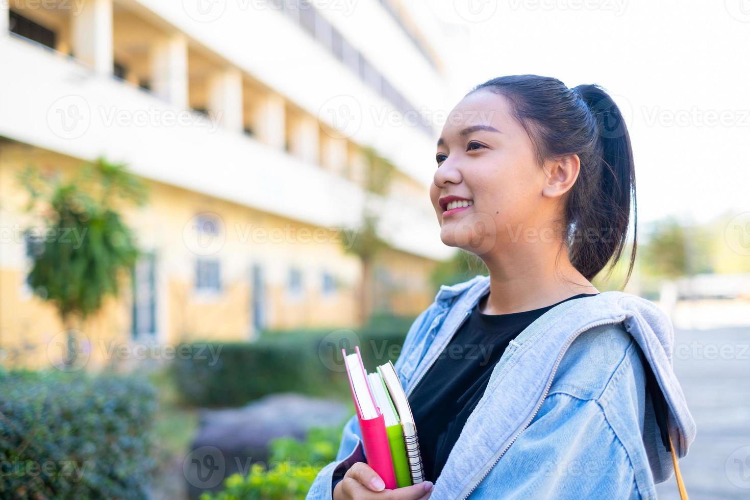 glad student flicka hålla bok och ryggsäck i skolan, asiatisk tjej. foto