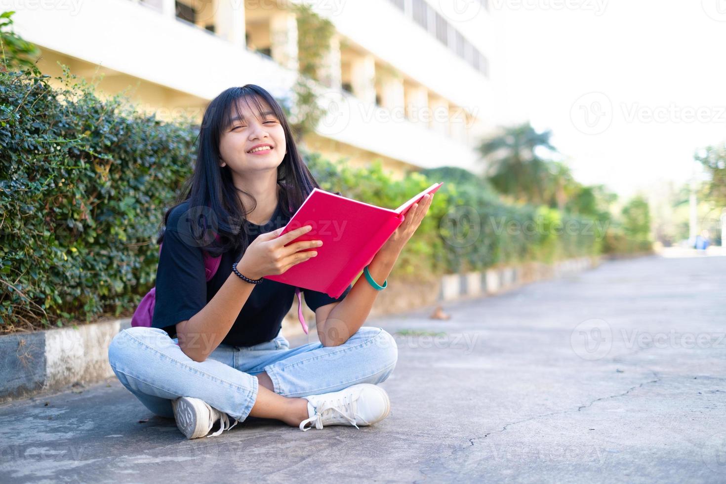 student ung flicka med rosa ryggsäck sitter vid foten med skolbakgrund. foto