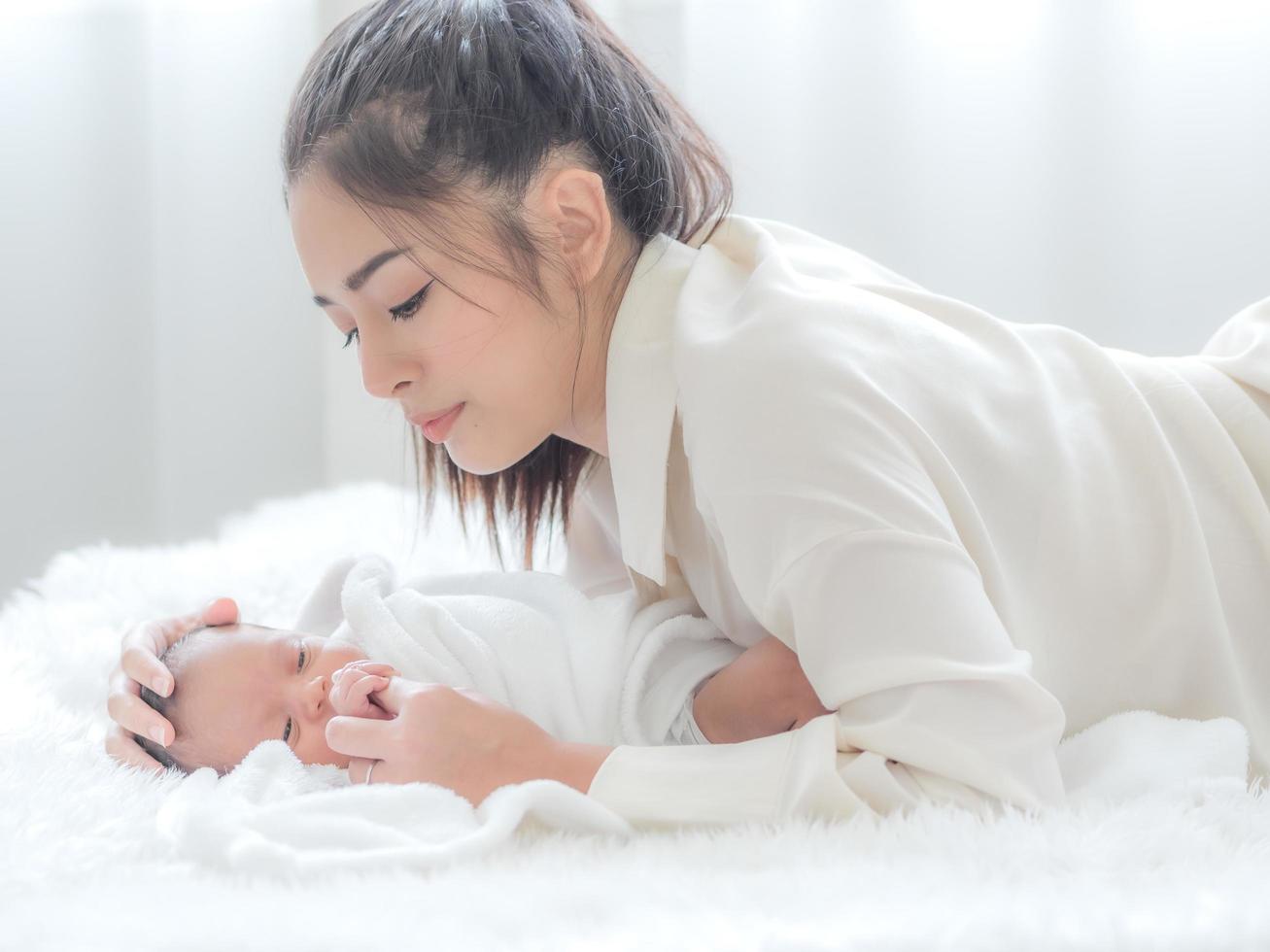 en vacker asiatisk kvinna tittar på sitt nyfödda barn med lycka och kärlek foto