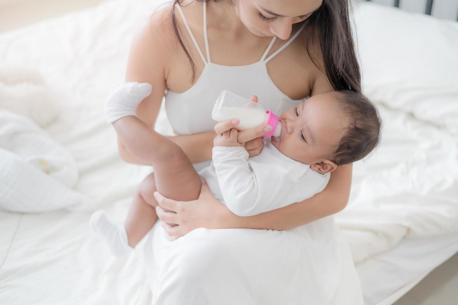 en vacker asiatisk kvinna som bär sitt nyfödda barn med kärlek och omtanke och matar henne med lycka foto