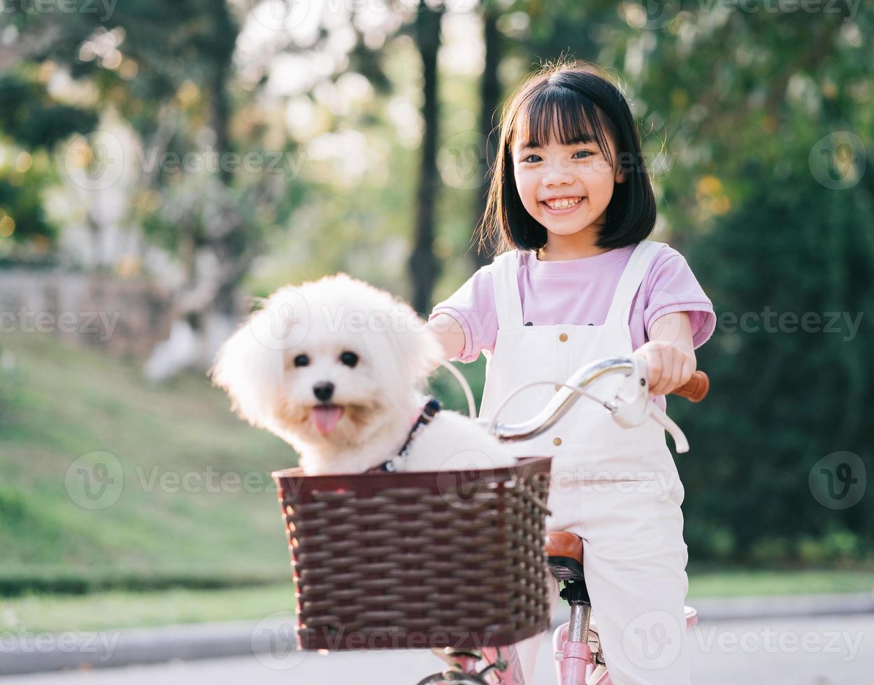 bild av asiatisk liten flicka som cyklar med sin hund i parken foto