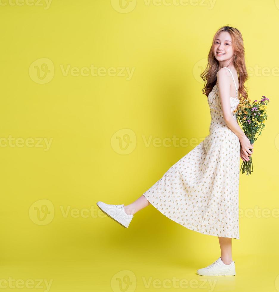 bild av ung asiatisk kvinna som håller blommor på gul bakgrund foto
