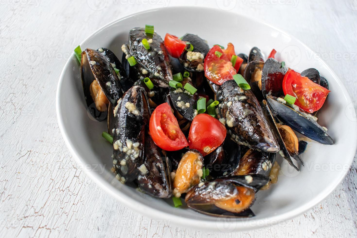 skaldjursrätt av kokta musslor med vitlök, tomater och salladslök foto