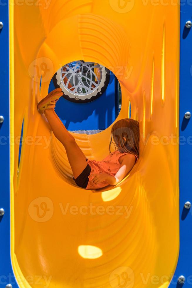 ung kaukasisk flicka avkopplande inuti ett gult plaströr på klätterställning foto
