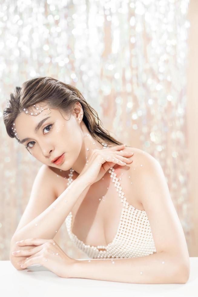 vacker ung asiatisk kvinna med ren fräsch hud med pärlor på glitterbakgrund. ansiktsvård, ansiktsbehandling, skönhet och spa, söta asiatiska kvinnor porträtt. foto