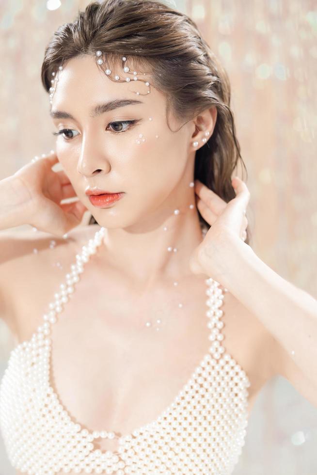 vacker ung asiatisk kvinna med ren fräsch hud med pärlor på glitterbakgrund. ansiktsvård, ansiktsbehandling, skönhet och spa, söta asiatiska kvinnor porträtt. foto