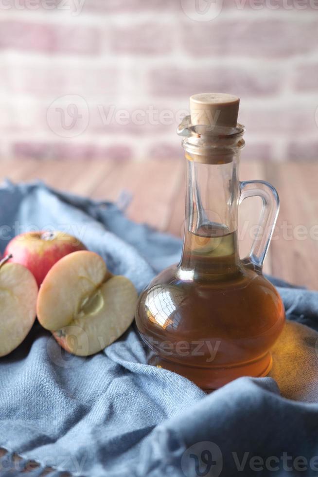 äppelvinäger i glasflaska med färskt grönt äpple på bordet foto