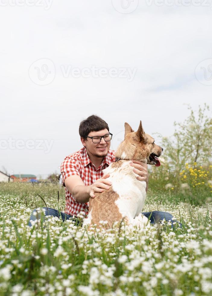 glad man sitter med blandras herdehund på grönt gräs i vårblommor foto