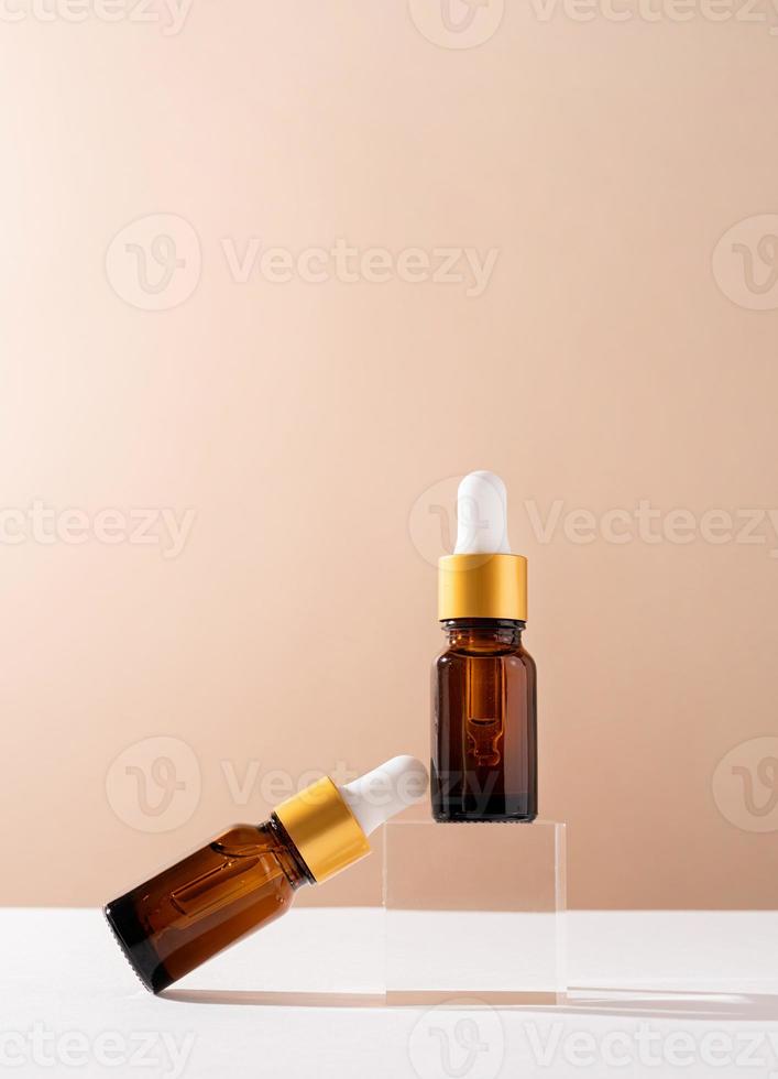 bärnstensfärgade droppflaskor i glas med en pipett med vit gummispets på glaspodium och beige bakgrund, mockupdesign foto