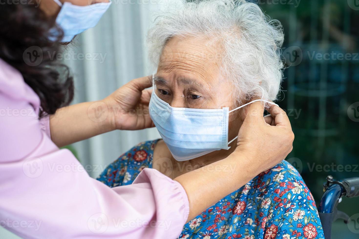 vårdgivare hjälpa asiatisk senior eller äldre kvinna som sitter i rullstol och bär en ansiktsmask för att skydda säkerhetsinfektion covid 19 coronavirus. foto