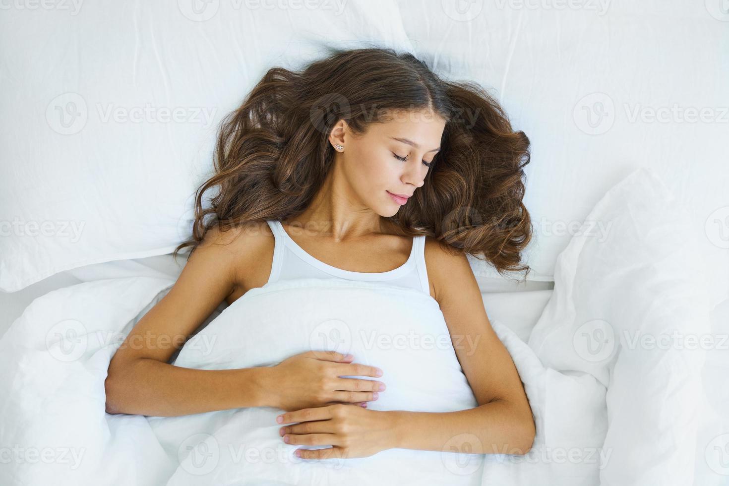 ovanifrån midja porträtt av vacker sovande kvinna i sängen. hona med långt hår vilande foto