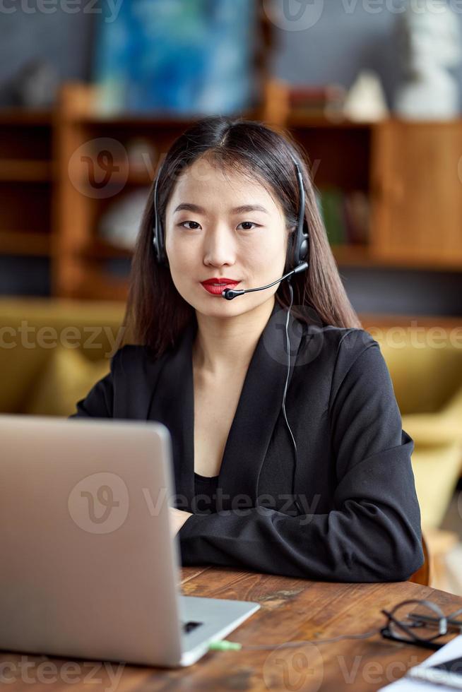 glad asiatisk affärskvinna i headset som talar genom konferenssamtal och videochatt foto