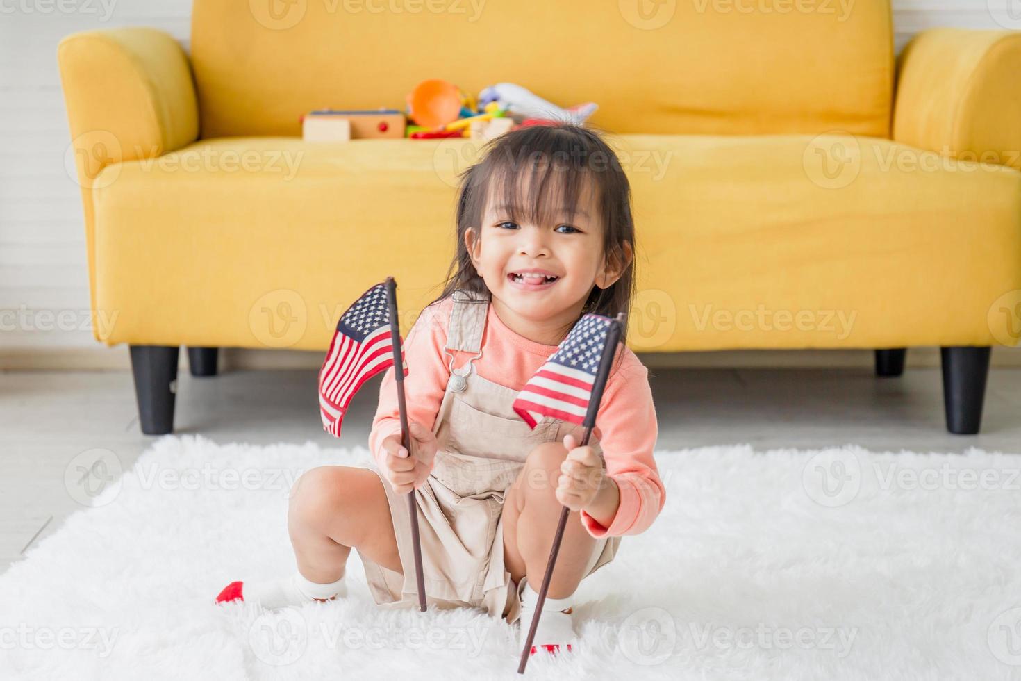 söt liten flicka med en liten nationell flagga i USA, barn flicka som leker i vardagsrummet foto