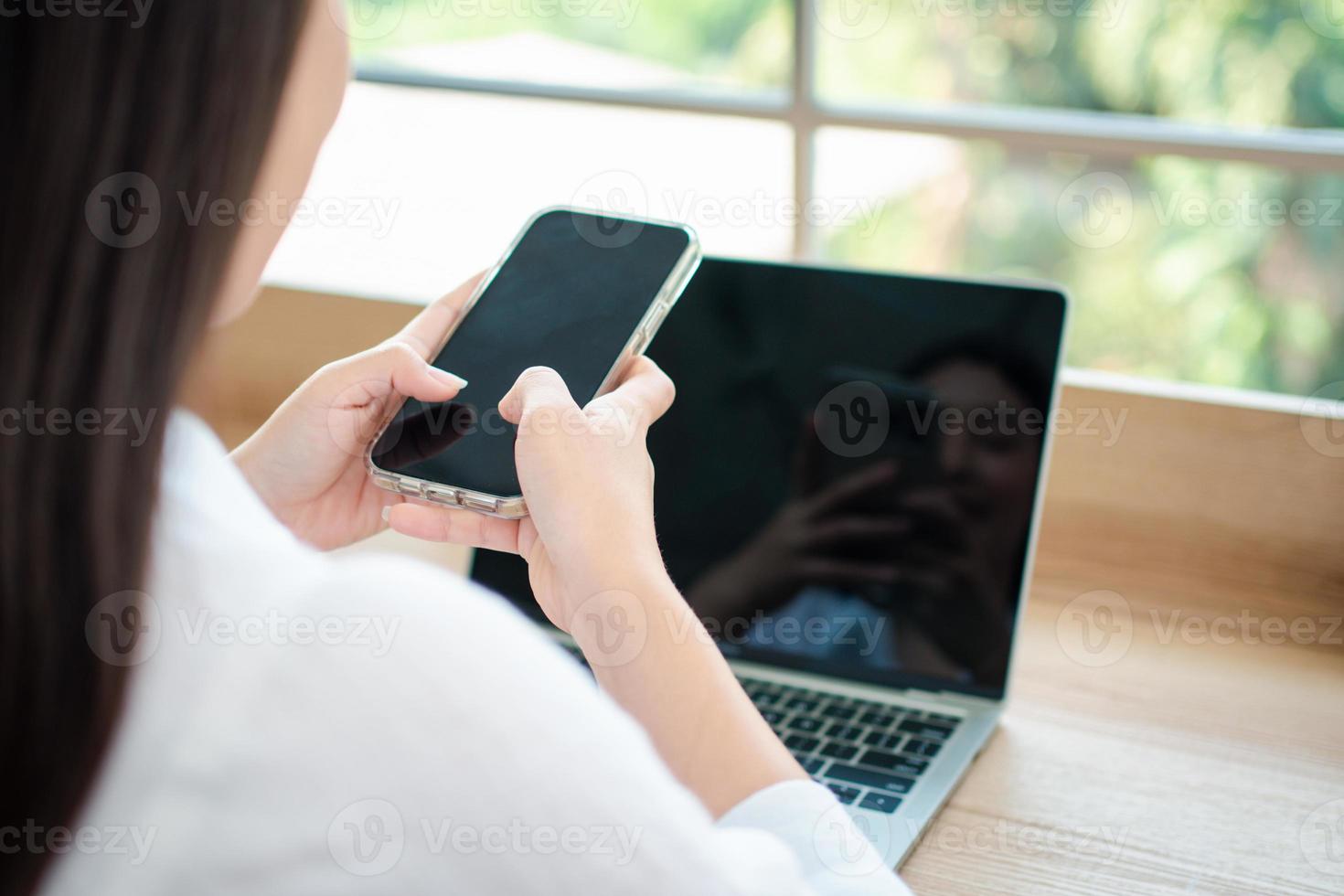 glad vacker asiatisk kvinna som arbetar på en bärbar dator och smartphone på hemmakontoret sitter vid bordet. glad kvinnlig professionell frilansare online med bärbar dator och smartphone-koncept. foto