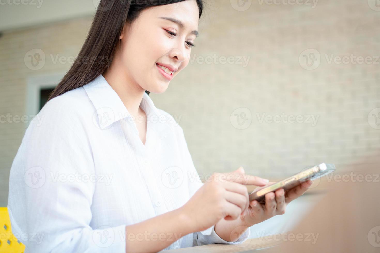 glad vacker asiatisk kvinna som arbetar på en bärbar dator och smartphone på hemmakontoret sitter vid bordet. glad kvinnlig professionell frilansare online med bärbar dator och smartphone-koncept. foto