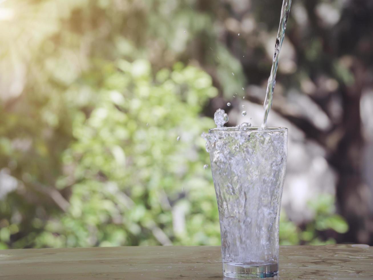 det rena vattnet från kanna i glas på träbord på naturbakgrund. foto