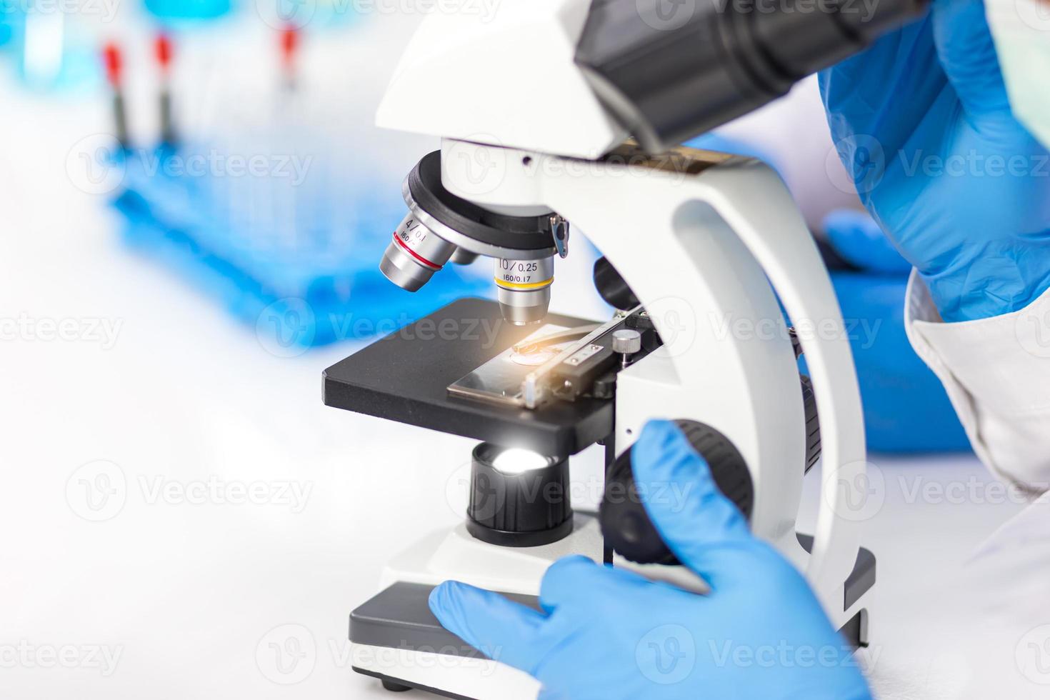 händerna på män som bär blå gummihandskar använder ett mikroskop för att arbeta i laboratoriet. foto