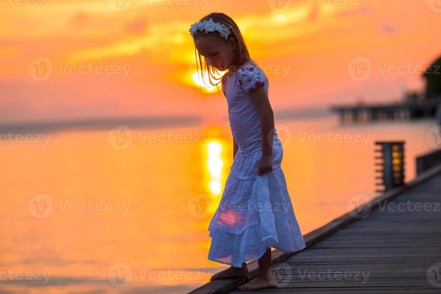 siluett av bedårande liten flicka på träbrygga i solnedgången foto