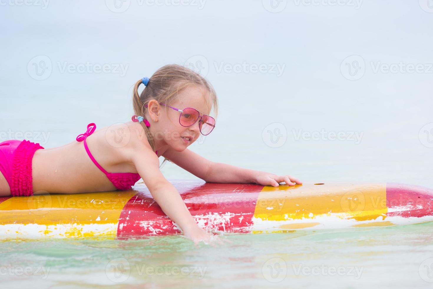 liten bedårande flicka på en surfbräda i det turkosa havet foto