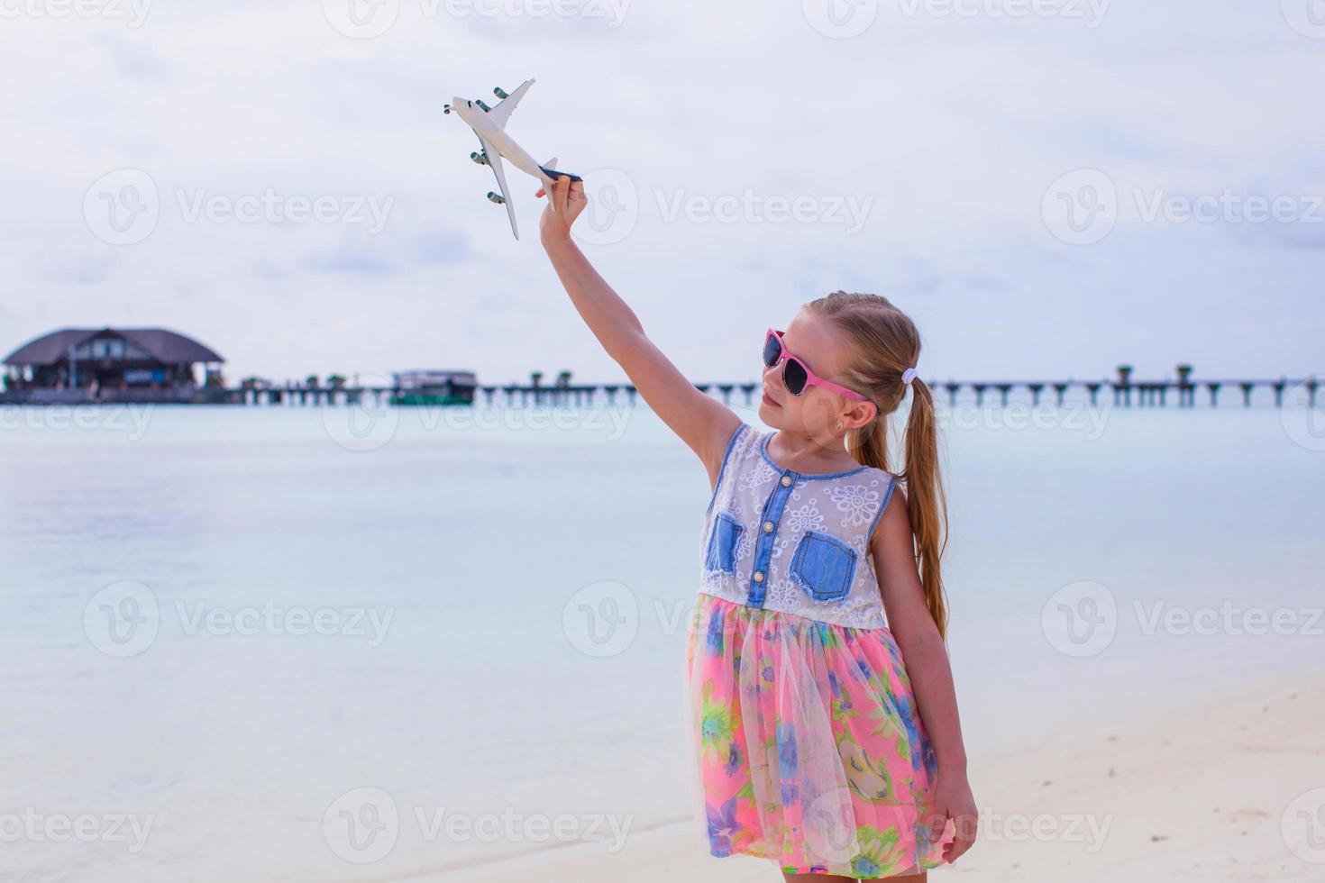 glad liten flicka med leksaksflygplan i händerna på den vita sandstranden foto