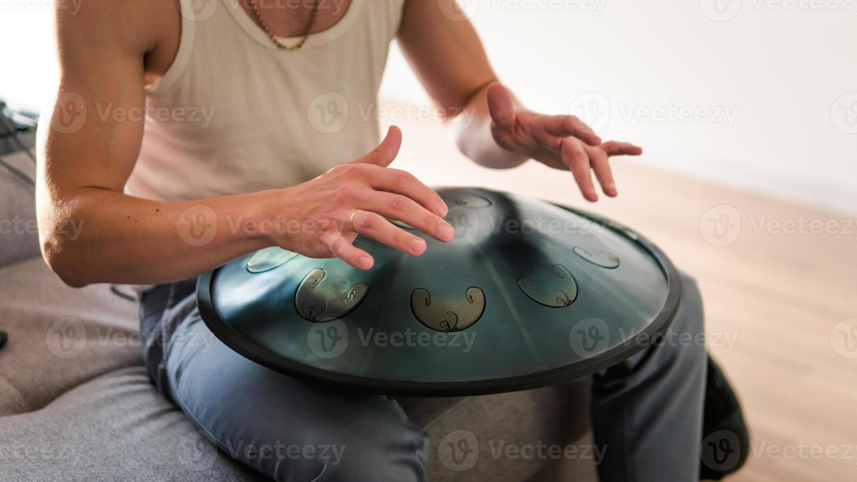 närbild av man händer spelar hänga trumma inomhus. ovanligt musikinstrument. foto