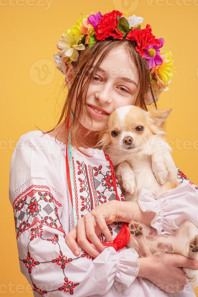 tonårsflicka med en krans på huvudet och klädd i en broderad skjorta med en chihuahuahund. sällskapsdjur. foto