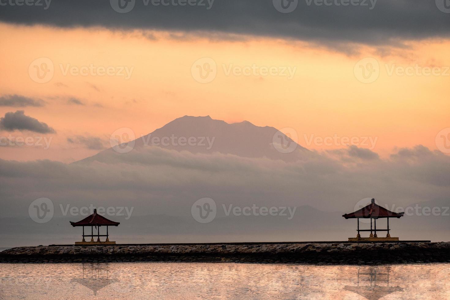 Montera vulkanen eller Gunung Agung med två paviljonger på bryggan vid solnedgången på Sanur Beach, Bali foto