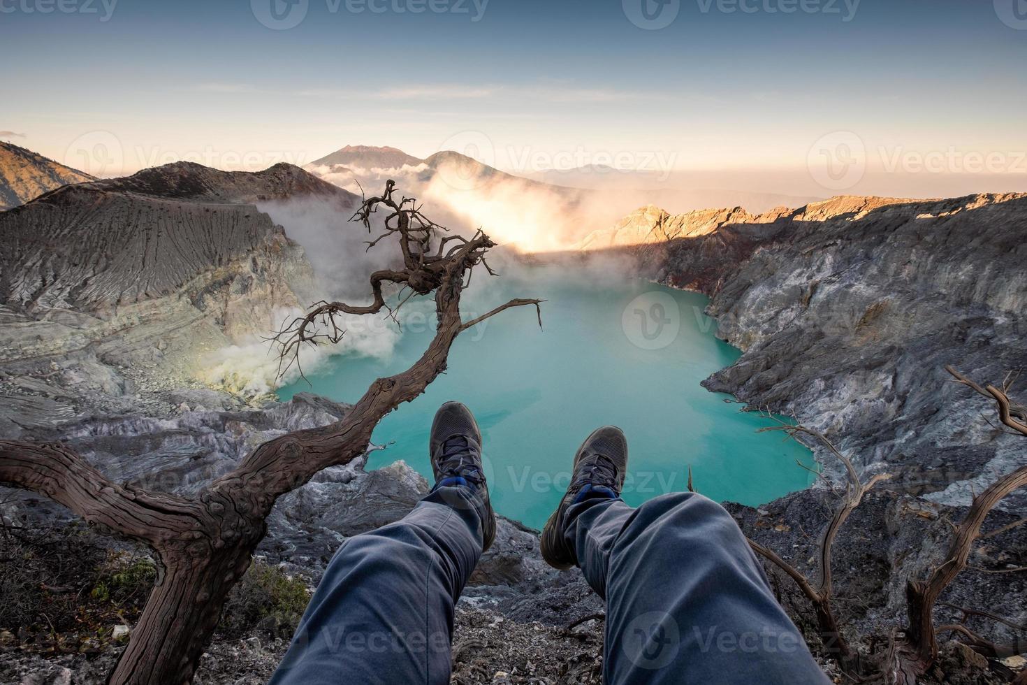 turist hängande ben på kratern kawah ijen med smaragd sjön vid soluppgången foto