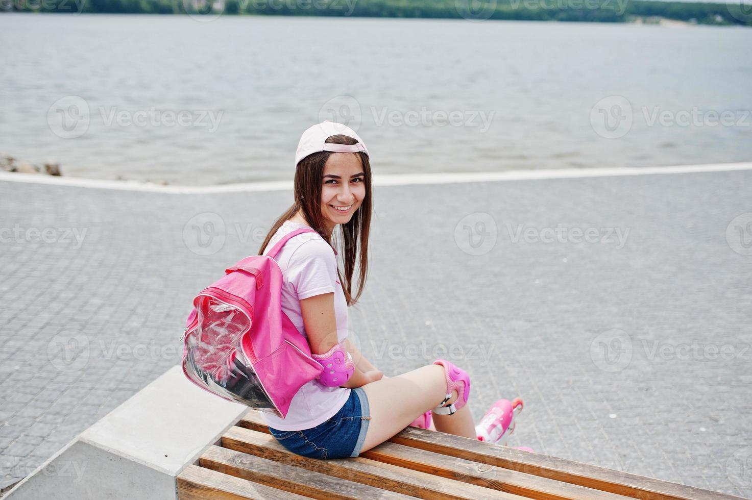 fantastisk ung kvinna i lediga kläder och keps sitter på bänken i skateparken med rullskridskor på. foto