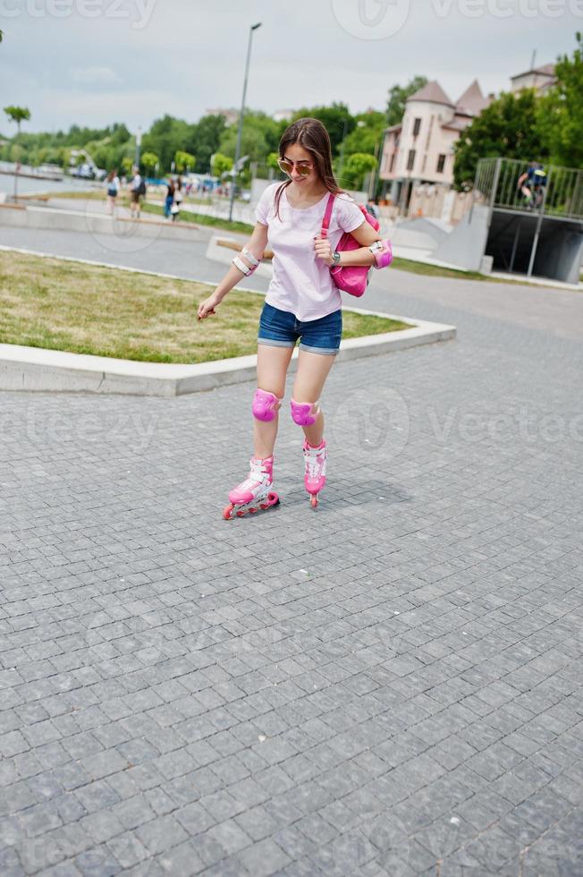 porträtt av en snygg ung kvinna i lediga kläder som åker rullskridskor på trottoaren i parken. foto