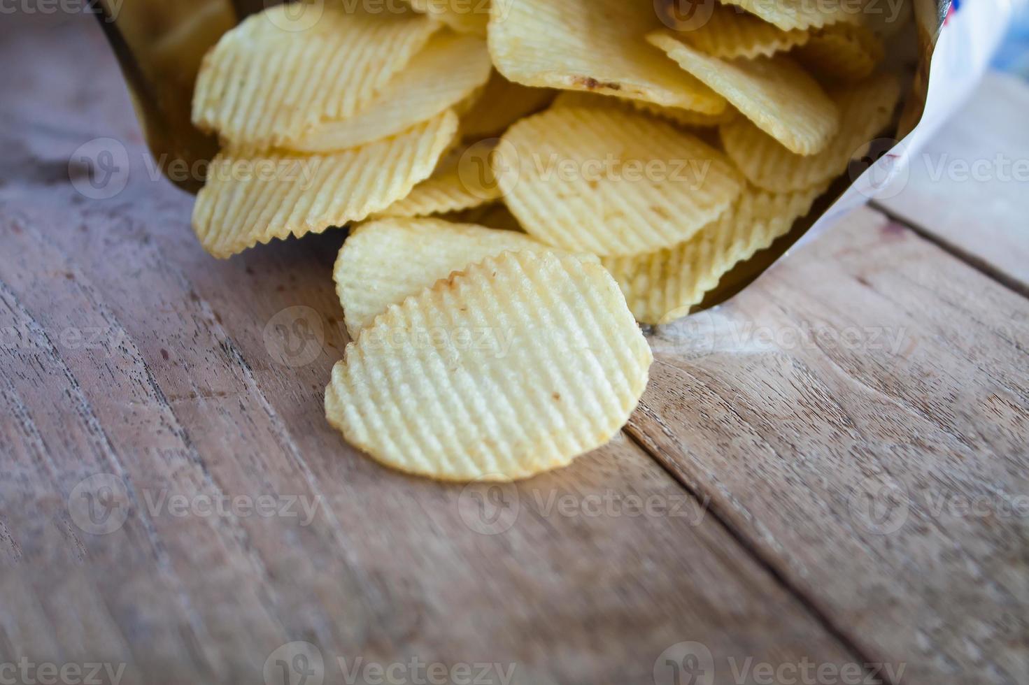 öppnad förpackning med potatischips över träbord foto